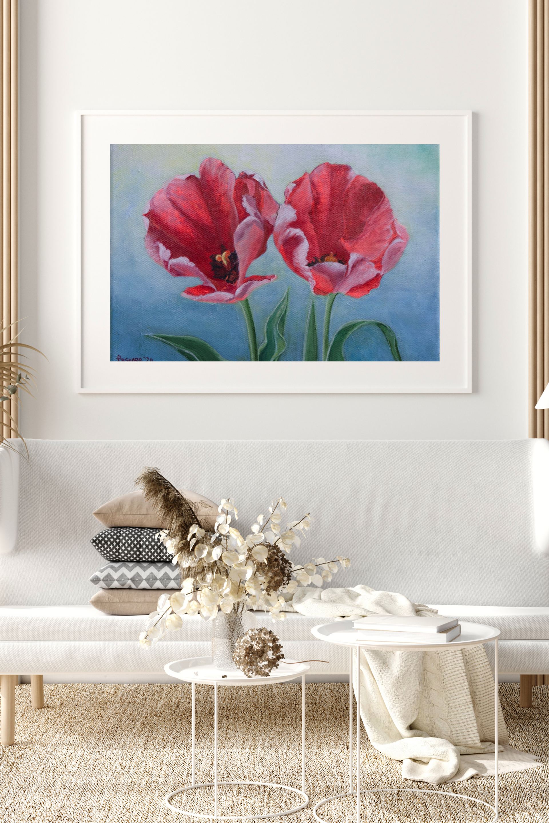 Framed artwork of red tulips on a wall above a white sofa with decorative items.