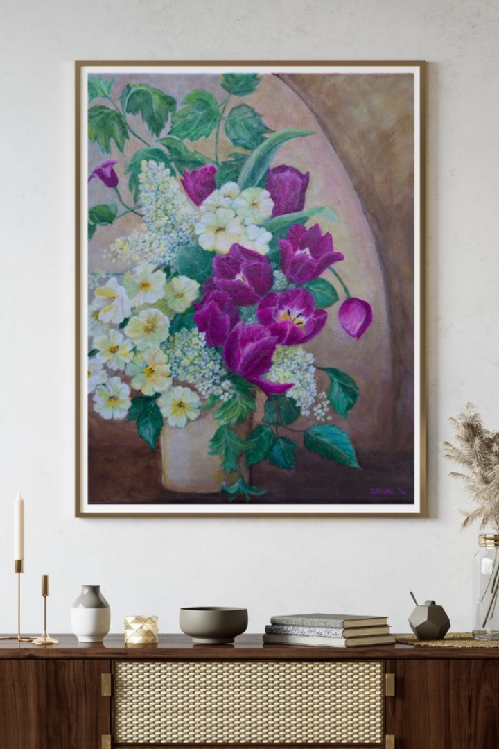 A framed floral painting hanging on a light wall above a wooden console table. The artwork shows a bouquet of white and purple flowers with green leaves against a warm brown and beige background.