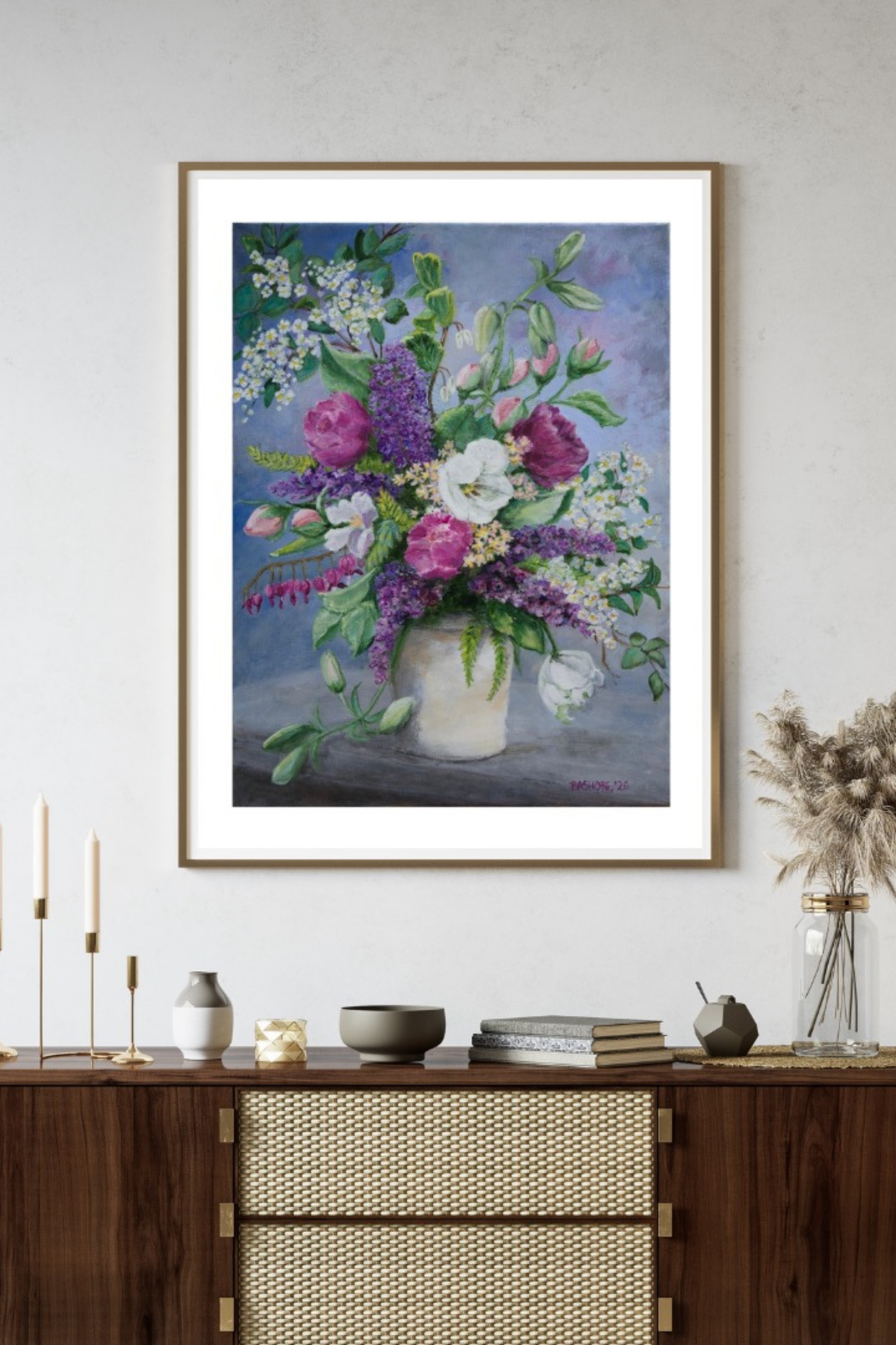 A framed floral painting hanging on a light gray wall above a wooden console table. The artwork shows a bouquet of pink, purple, white, and green flowers in a white vase against a soft blue-gray background.